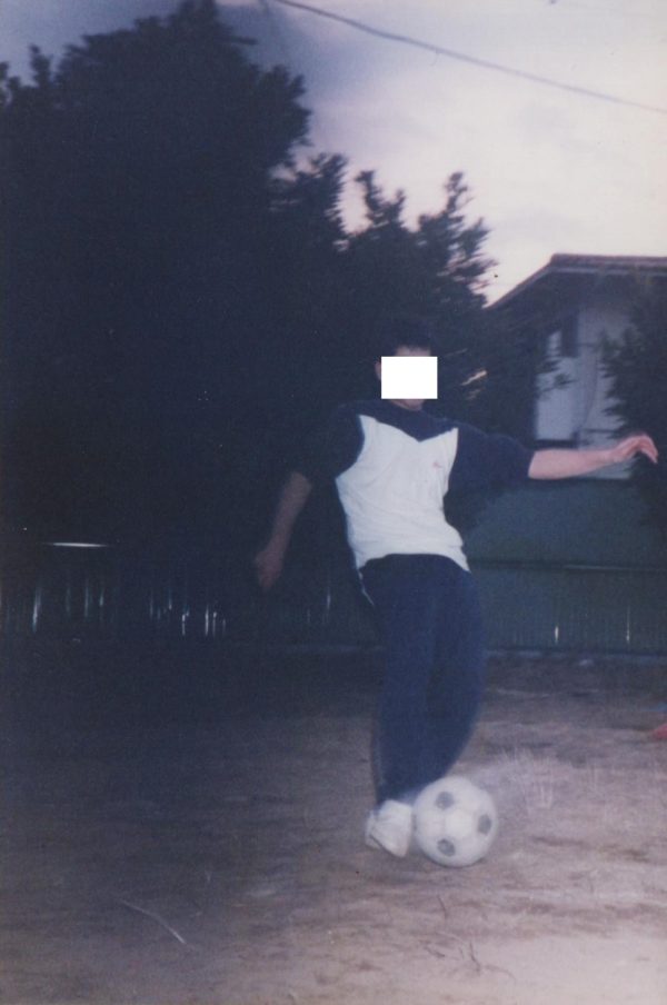 空き地でサッカーボールを蹴っている男性の画像